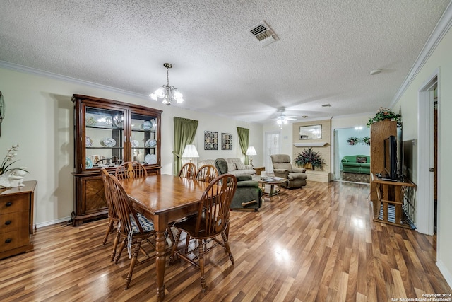 dining space with a textured ceiling, ceiling fan with notable chandelier, hardwood / wood-style flooring, and crown molding