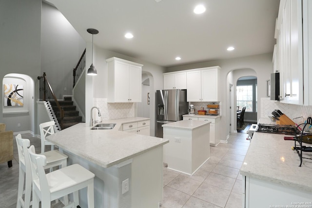 kitchen with sink, a kitchen island, stainless steel fridge, decorative light fixtures, and white cabinets