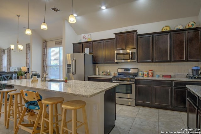 kitchen featuring decorative backsplash, vaulted ceiling, stainless steel appliances, and an island with sink