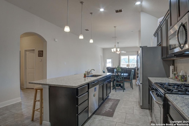 kitchen featuring light stone countertops, appliances with stainless steel finishes, backsplash, a center island with sink, and decorative light fixtures