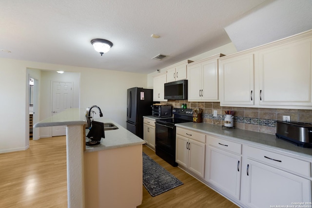 kitchen featuring white cabinetry, sink, light hardwood / wood-style floors, a center island with sink, and black appliances