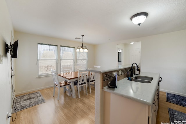 kitchen featuring light wood-type flooring, sink, pendant lighting, a center island with sink, and a notable chandelier