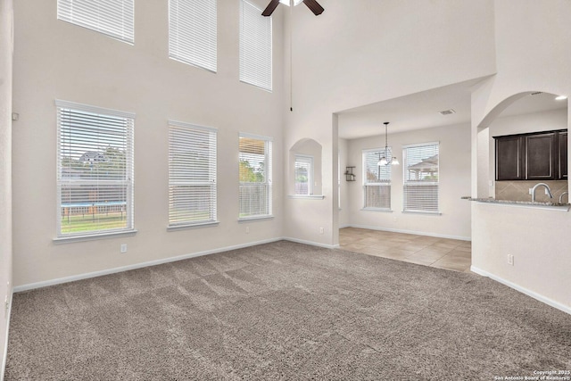 unfurnished living room featuring plenty of natural light, light colored carpet, and ceiling fan with notable chandelier