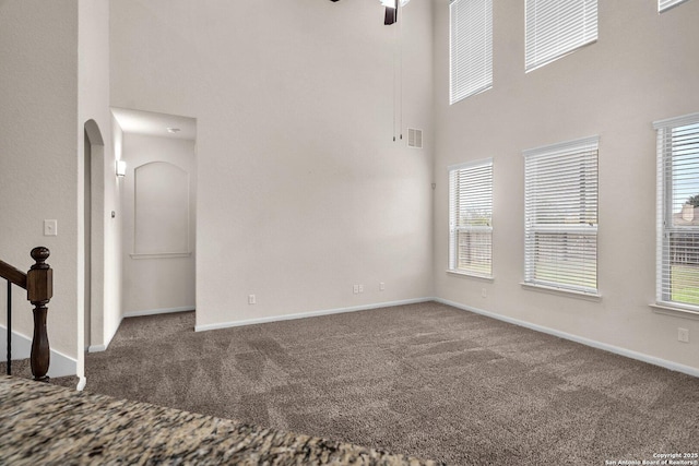 empty room with carpet flooring, ceiling fan, and a high ceiling