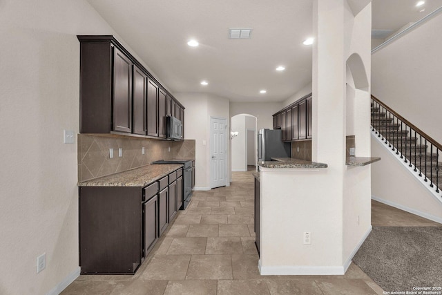 kitchen featuring appliances with stainless steel finishes, dark brown cabinetry, light stone counters, and backsplash