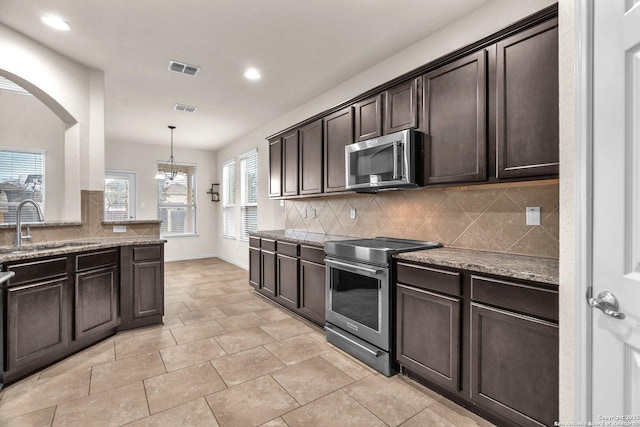 kitchen with appliances with stainless steel finishes, tasteful backsplash, dark brown cabinets, a notable chandelier, and hanging light fixtures