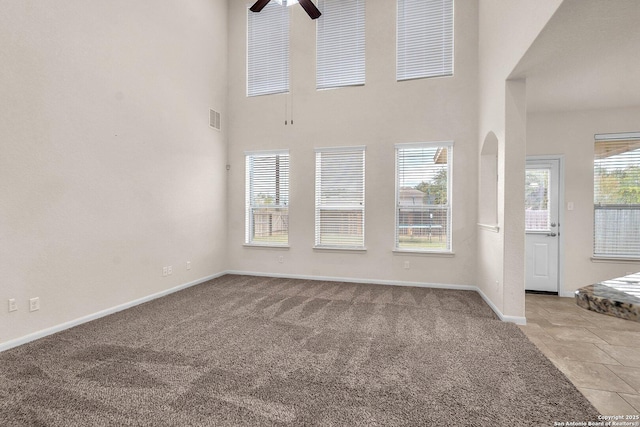 unfurnished living room featuring a high ceiling, light colored carpet, and ceiling fan