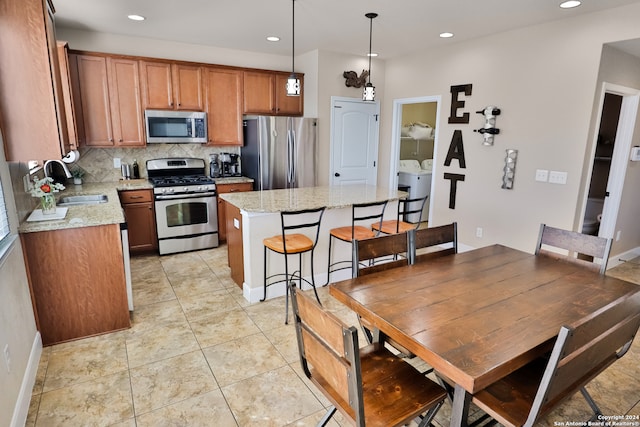 kitchen featuring sink, hanging light fixtures, a kitchen island, light stone counters, and stainless steel appliances