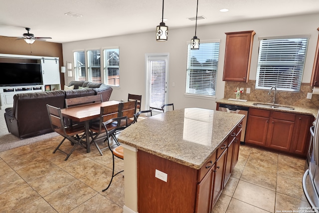 kitchen featuring decorative light fixtures, a center island, light stone counters, and sink