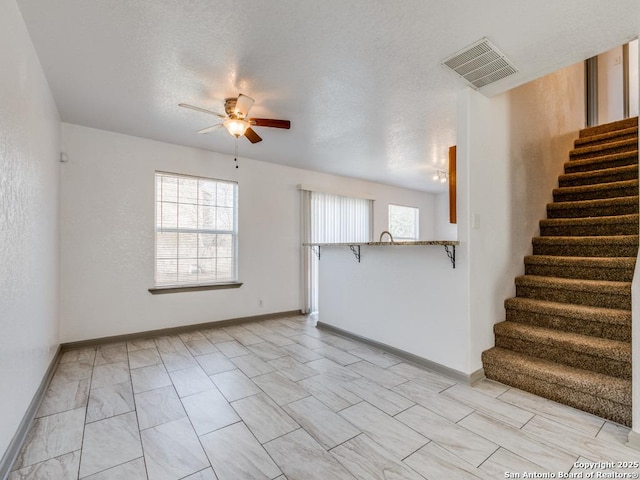 unfurnished living room featuring ceiling fan and a textured ceiling