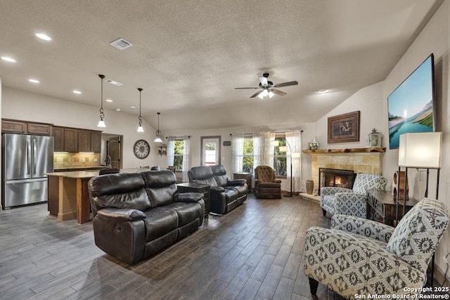 living room with a textured ceiling, ceiling fan, a fireplace, and vaulted ceiling