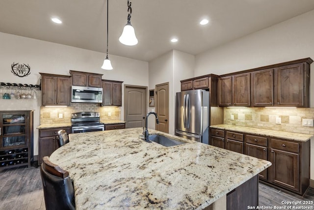 kitchen featuring sink, hanging light fixtures, stainless steel appliances, an island with sink, and dark brown cabinets