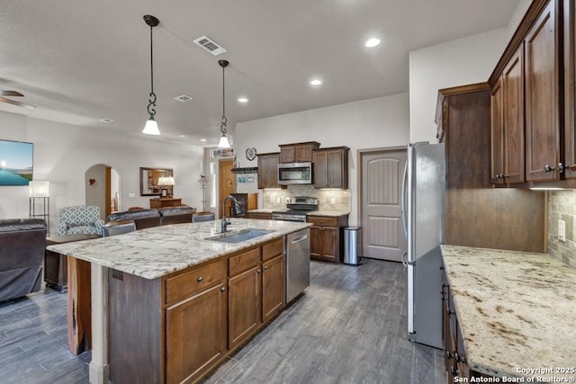 kitchen with a kitchen island with sink, sink, decorative backsplash, light stone counters, and stainless steel appliances