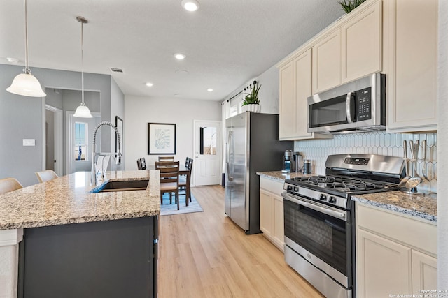 kitchen with decorative backsplash, appliances with stainless steel finishes, light stone countertops, a kitchen island with sink, and decorative light fixtures