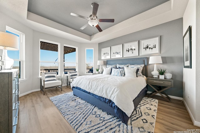 bedroom featuring a tray ceiling, ceiling fan, and light wood-type flooring