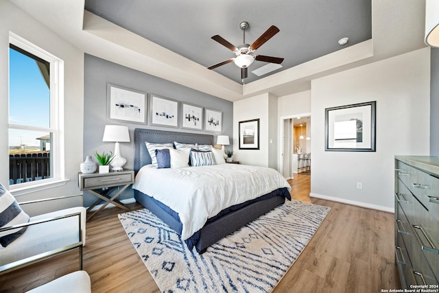 bedroom with ceiling fan, light hardwood / wood-style flooring, and a tray ceiling