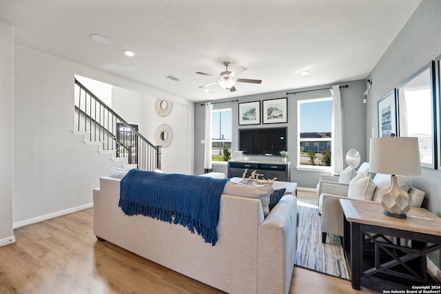 living room featuring a textured ceiling, light wood-type flooring, and ceiling fan