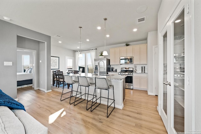 kitchen featuring decorative light fixtures, light wood-type flooring, stainless steel appliances, and a center island with sink