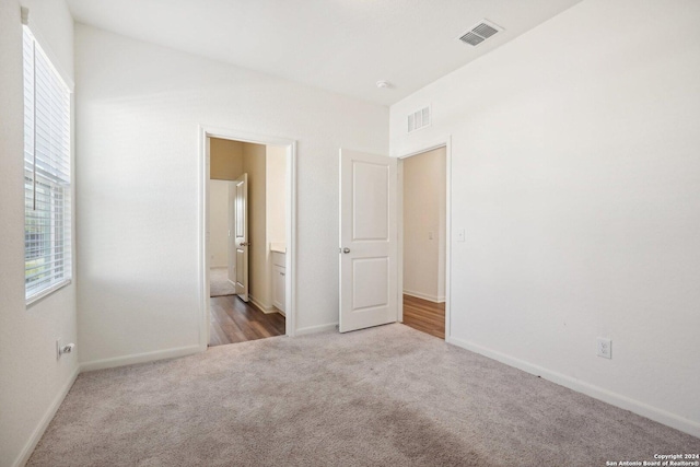 unfurnished bedroom with light colored carpet, connected bathroom, and multiple windows