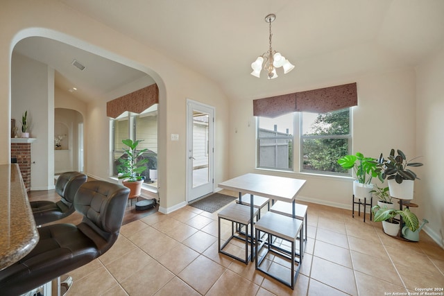 dining space featuring a brick fireplace, a notable chandelier, light tile patterned floors, and vaulted ceiling