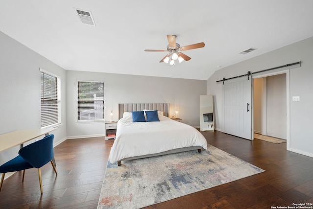 bedroom with ceiling fan, a barn door, dark hardwood / wood-style floors, and vaulted ceiling