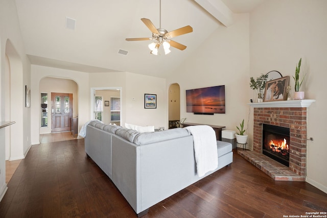 living room featuring beam ceiling, ceiling fan, dark wood-type flooring, and a brick fireplace