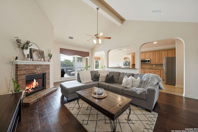 living room featuring wood-type flooring, lofted ceiling with beams, a brick fireplace, and ceiling fan