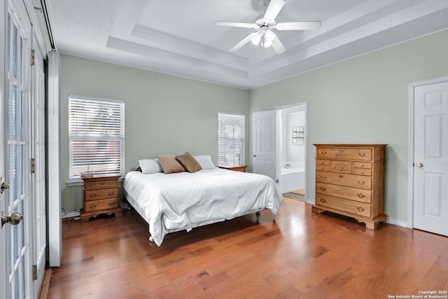 bedroom featuring ensuite bath, a raised ceiling, ceiling fan, and dark wood-type flooring