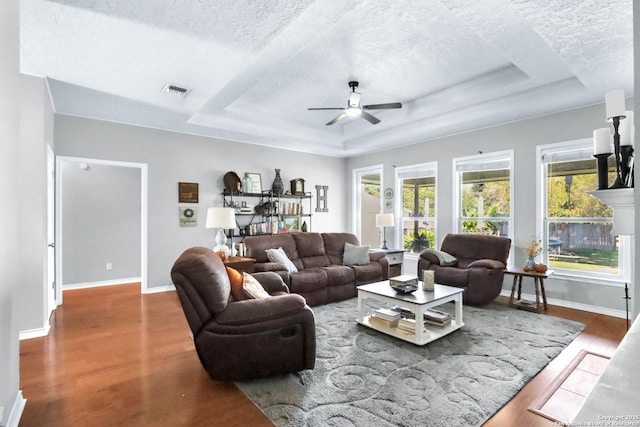 living room with a textured ceiling, a tray ceiling, hardwood / wood-style flooring, and ceiling fan