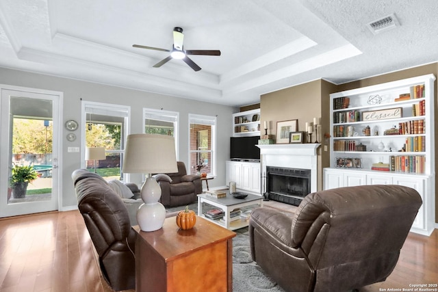 living room featuring a textured ceiling, a tray ceiling, hardwood / wood-style flooring, and ceiling fan