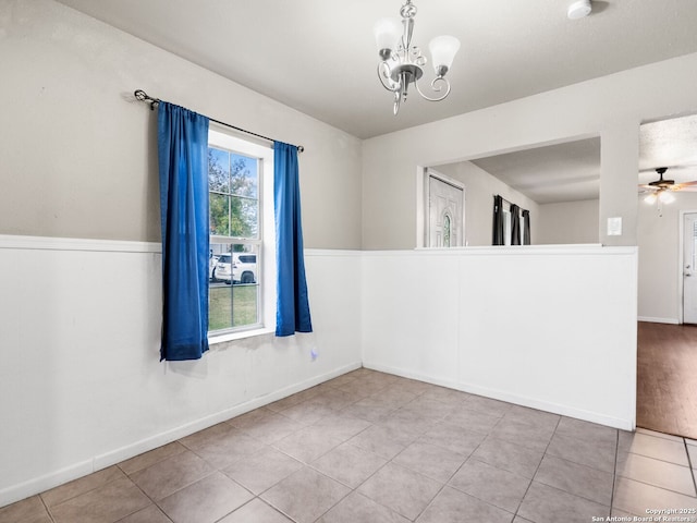 tiled empty room featuring ceiling fan with notable chandelier