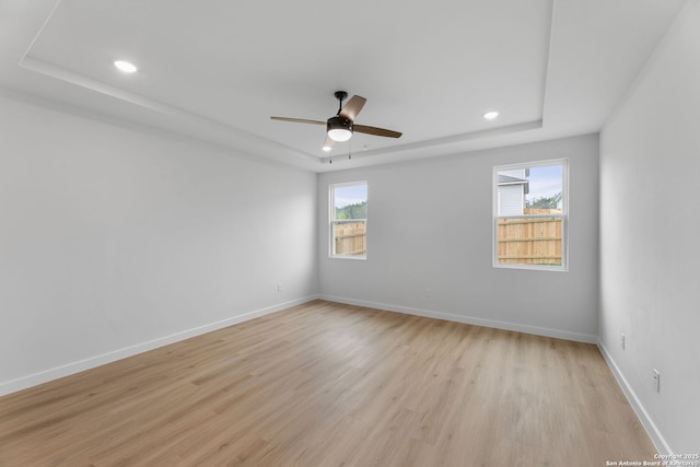 empty room with baseboards, light wood-type flooring, a ceiling fan, and a raised ceiling