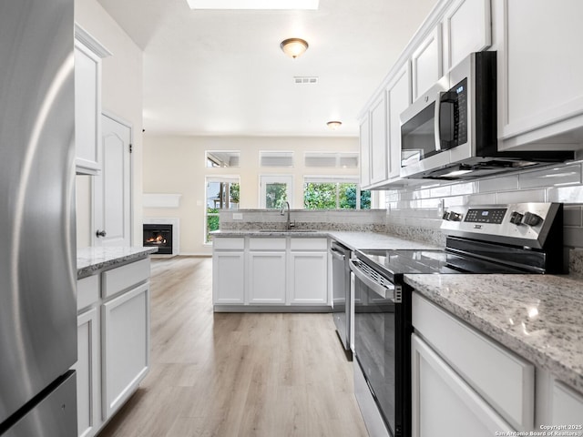 kitchen with sink, stainless steel appliances, light stone counters, white cabinets, and light wood-type flooring