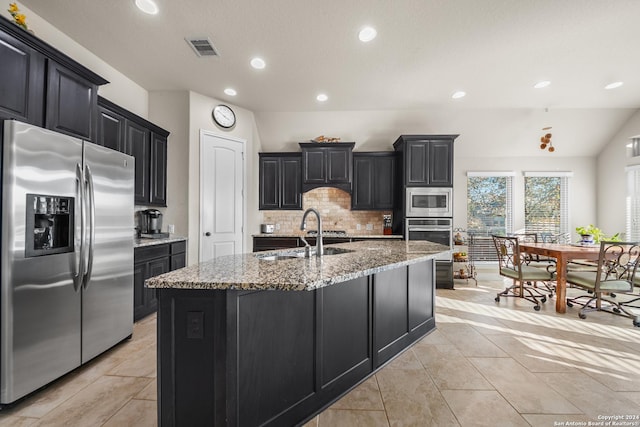 kitchen featuring decorative backsplash, lofted ceiling, stainless steel appliances, and an island with sink