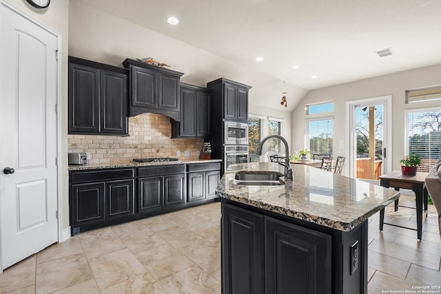 kitchen featuring appliances with stainless steel finishes, backsplash, vaulted ceiling, sink, and a center island with sink