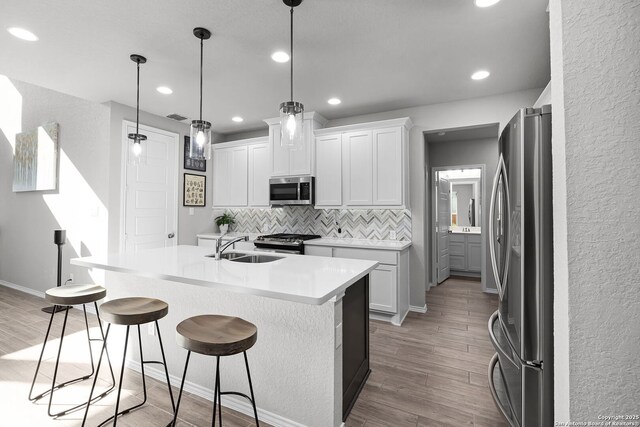 kitchen with hanging light fixtures, stainless steel appliances, decorative backsplash, a center island with sink, and white cabinets