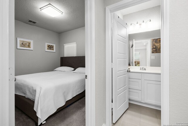 bedroom featuring ensuite bathroom, sink, light tile patterned floors, and a textured ceiling