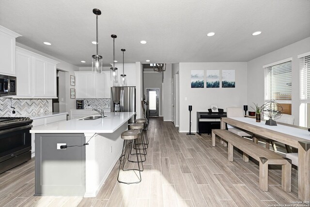 kitchen featuring a center island with sink, white cabinets, hanging light fixtures, sink, and appliances with stainless steel finishes