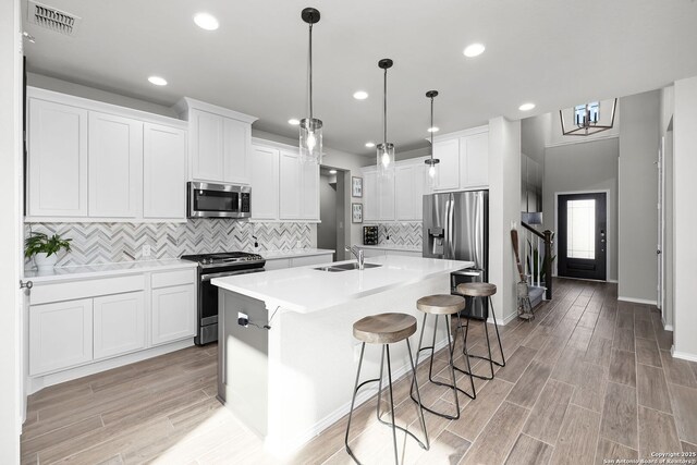 kitchen with hanging light fixtures, a kitchen bar, a center island with sink, white cabinets, and appliances with stainless steel finishes