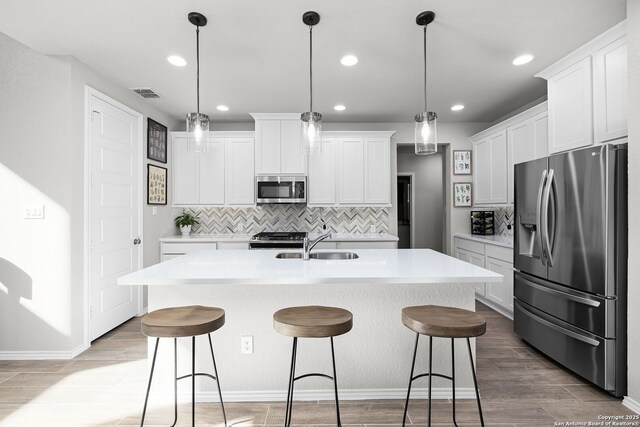 kitchen with appliances with stainless steel finishes, sink, pendant lighting, white cabinetry, and an island with sink