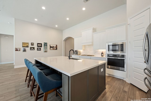 kitchen with a center island with sink, sink, appliances with stainless steel finishes, white cabinetry, and a breakfast bar area