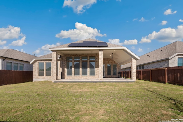 rear view of property featuring a yard, a patio, solar panels, and ceiling fan