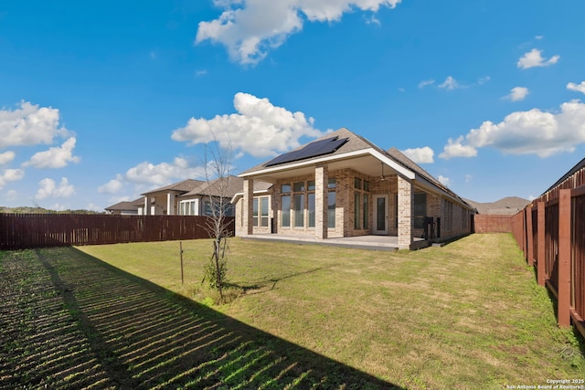 back of house featuring a patio area, a yard, and solar panels