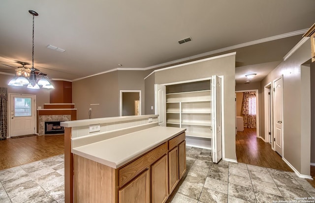 kitchen with ceiling fan, crown molding, a center island, hanging light fixtures, and a tiled fireplace