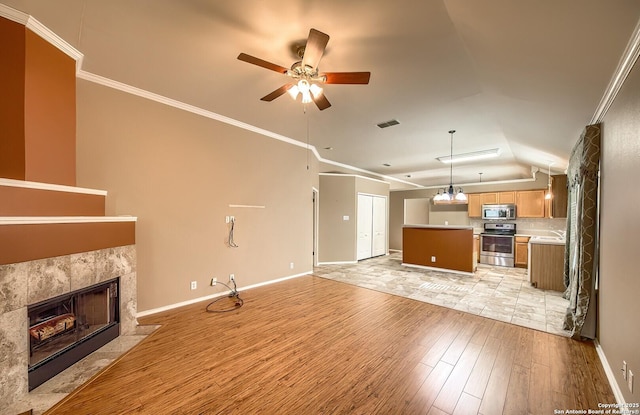 unfurnished living room featuring ceiling fan, crown molding, lofted ceiling, a tiled fireplace, and light wood-type flooring