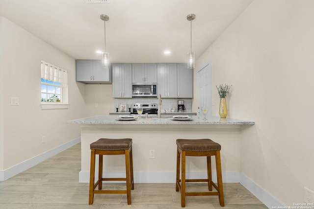 kitchen with light stone countertops, appliances with stainless steel finishes, kitchen peninsula, tasteful backsplash, and decorative light fixtures