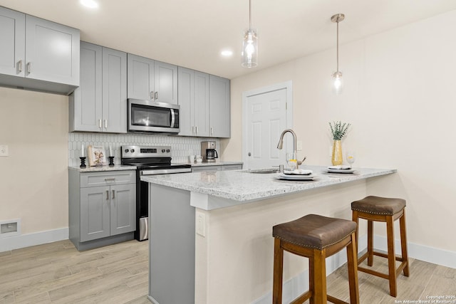 kitchen with light stone countertops, sink, hanging light fixtures, stainless steel appliances, and backsplash