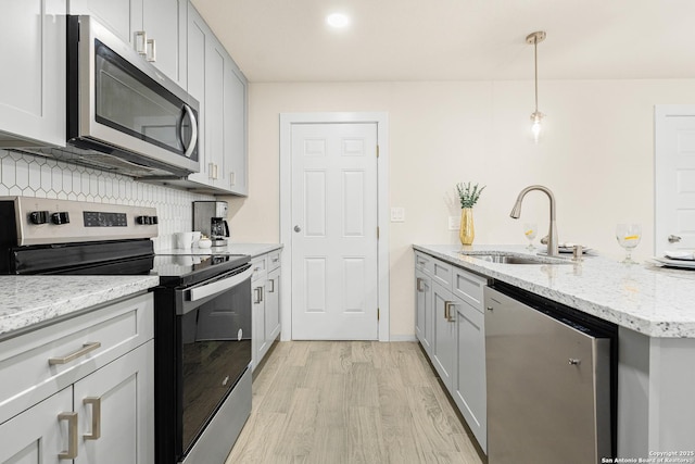 kitchen featuring backsplash, light stone counters, stainless steel appliances, sink, and decorative light fixtures