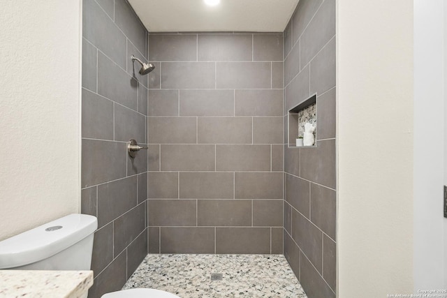 bathroom with a tile shower and toilet