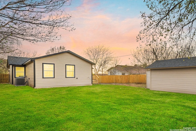 back house at dusk featuring a lawn and central AC unit